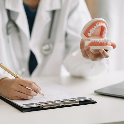 Dentist holding model teeth filling out form on clipboard with pen