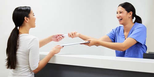 Smiling dental assistant handing patient form