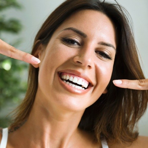 Woman pointing to her smile after porcelain veneers treatment