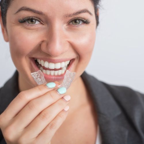 Smiling woman holding Invisalign clear aligner tray