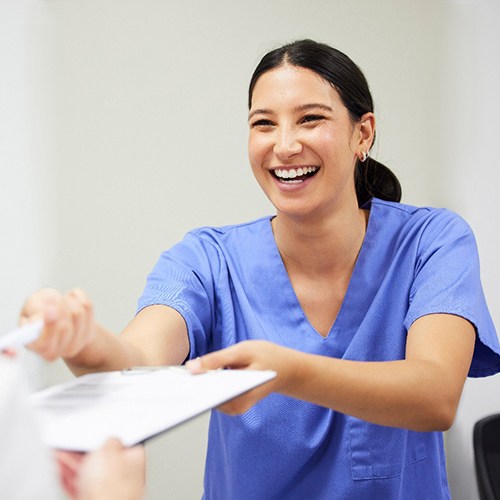 a dental assistant handing a patient forms on a clipboard