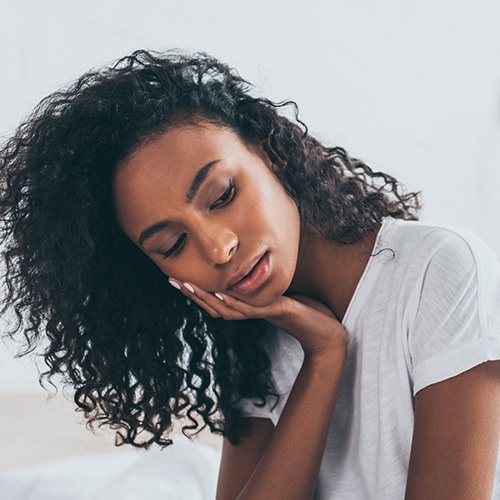 Woman holding cheek in pain before emergency dentistry