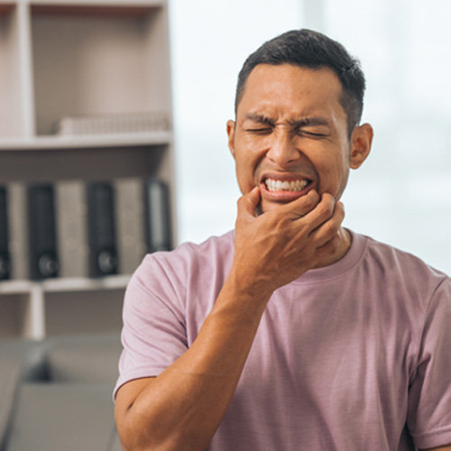 Man in pink shirt holding hand to jaw in pain