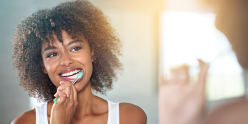 Woman in white tank top brushing teeth in front of mirror
