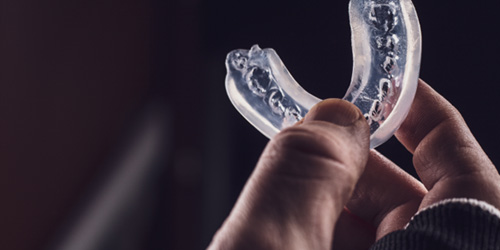 Hand with fingerless gloves holding transparent mouthguard