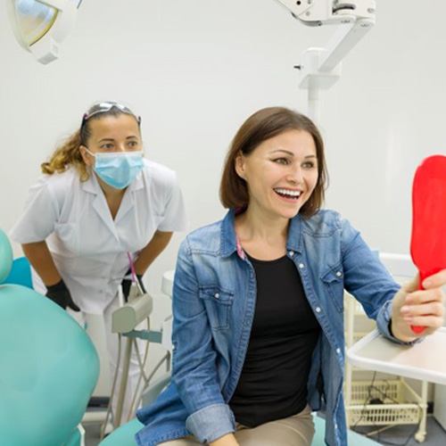 Dental patient holding mirror, admiring her teeth