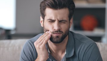 Man in need of emergency dentistry holding cheek in pain